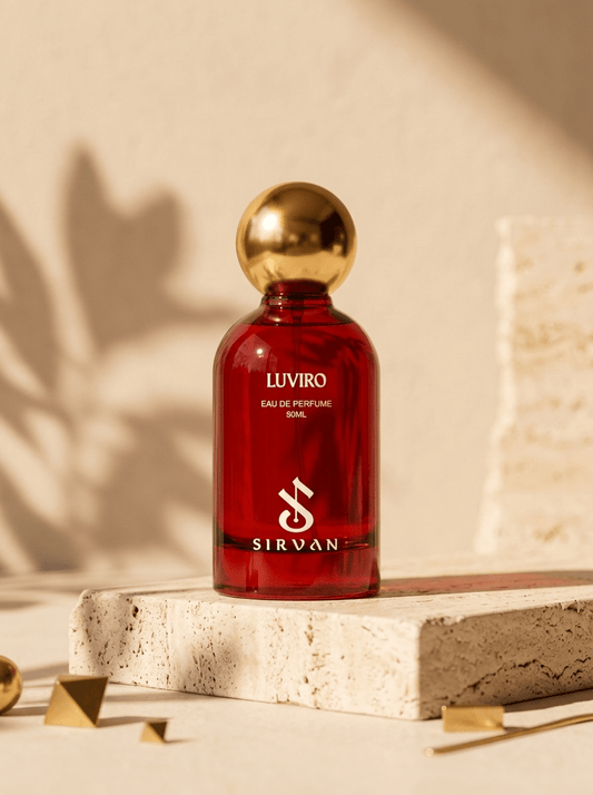 A red SIRVAN Luviro — Eau de Parfum bottle with a gold cap sits on stone, glowing in gentle sunlight.